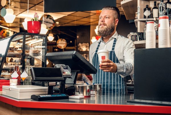 A man at the counter using cash register in a coffee shop.