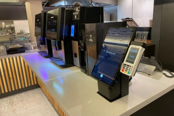 Catering kiosks with touchscreen ordering and card payment terminals in a busy hospitality venue.